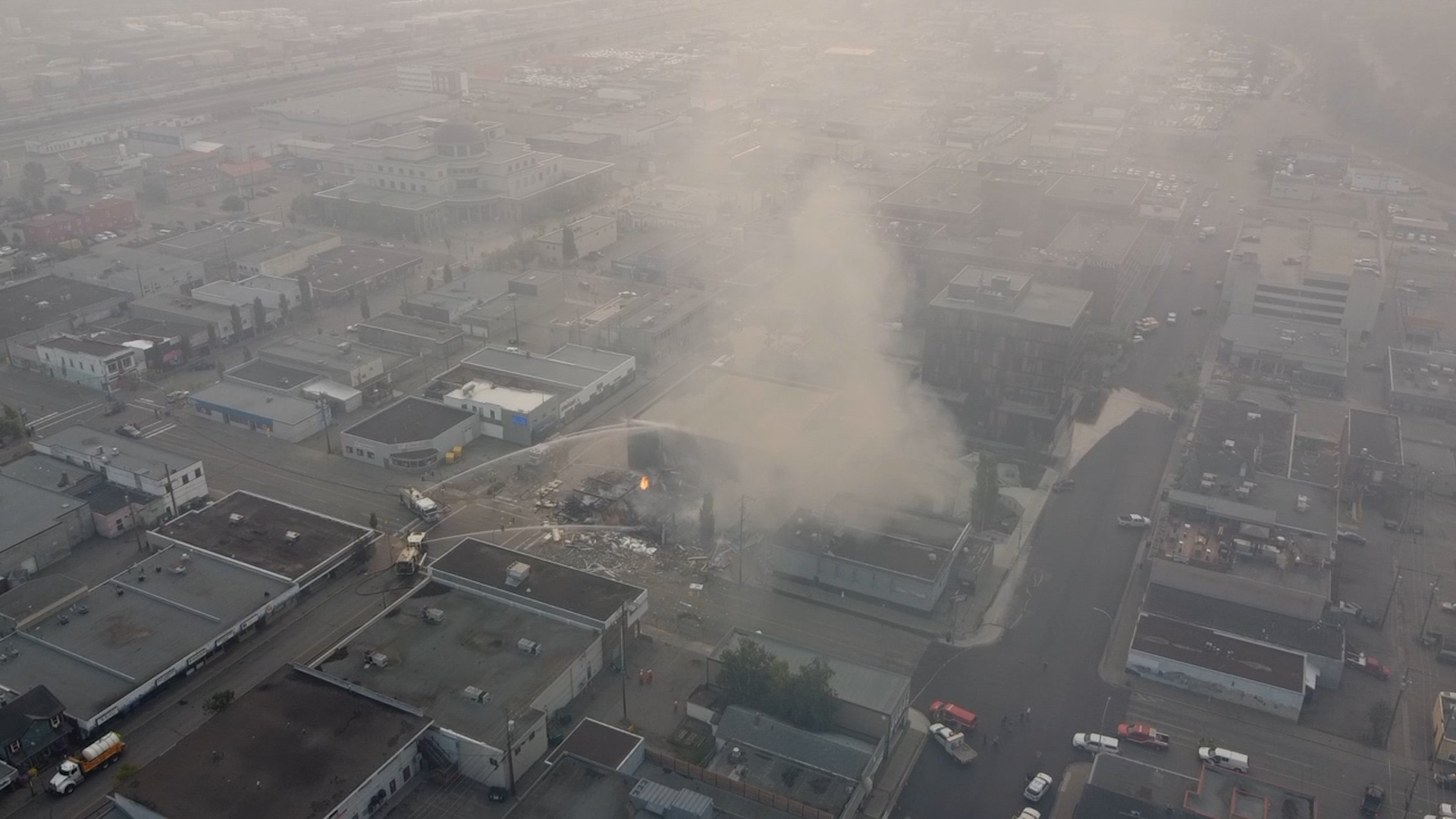 Aerial shot of a plume of smoke rising from a downtown building. Smoke fills the air.