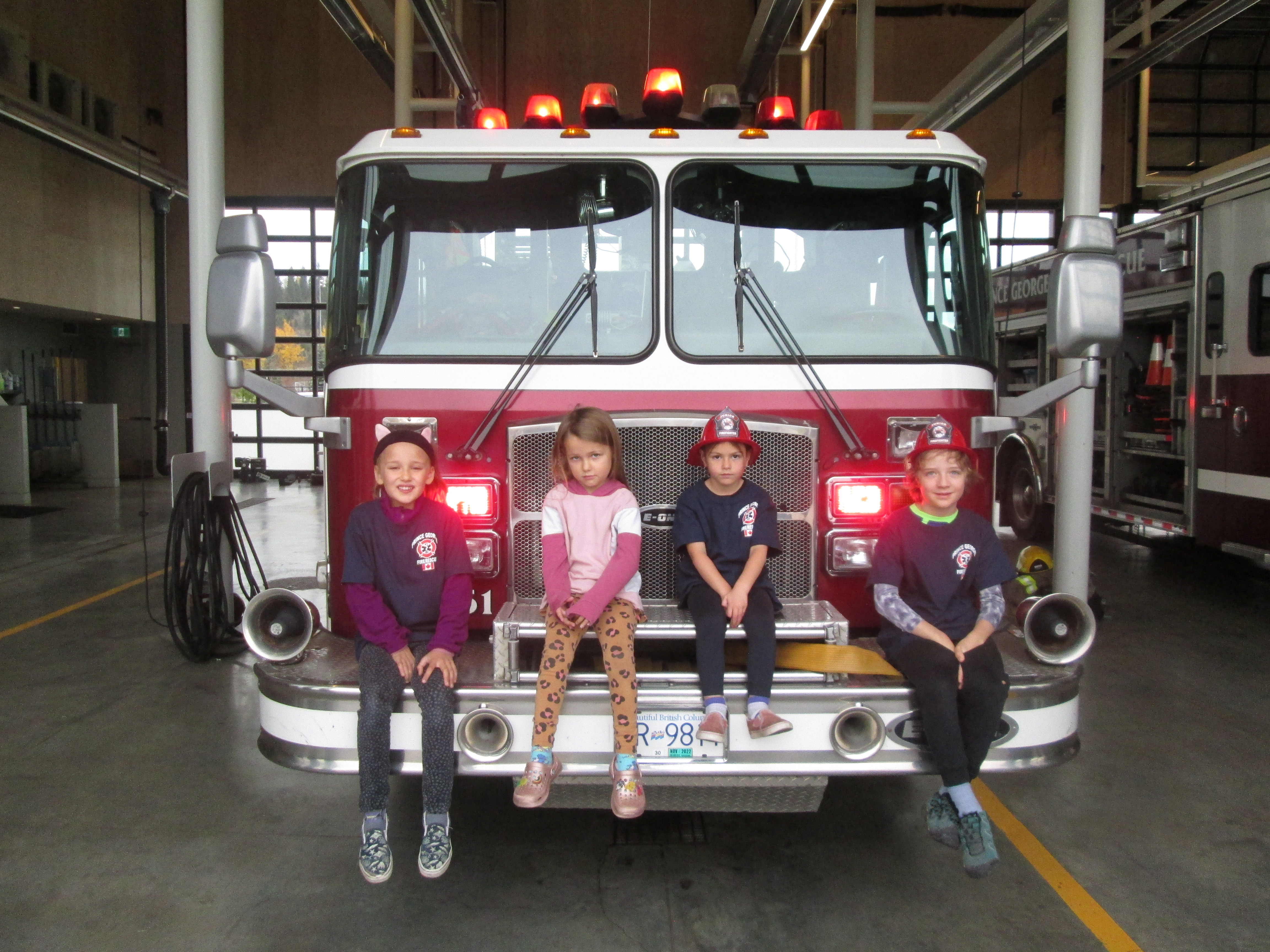 Four primary school aged children sitting on the front of a fire truck