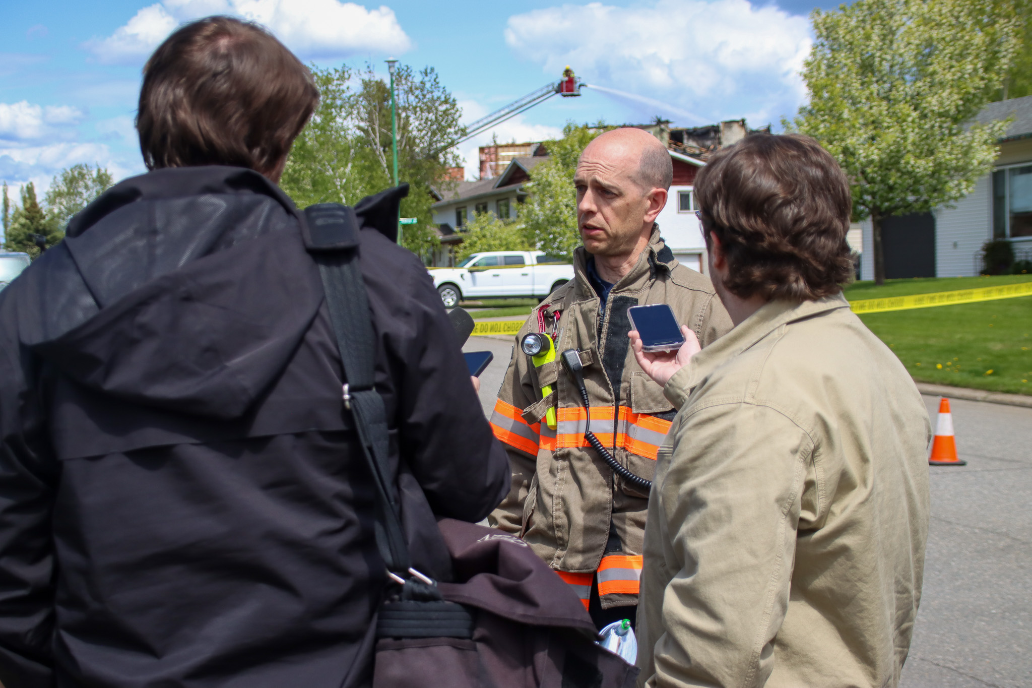 a photo show the back of two men's heads with a person between them in fire fighter uniform talking into a microphone