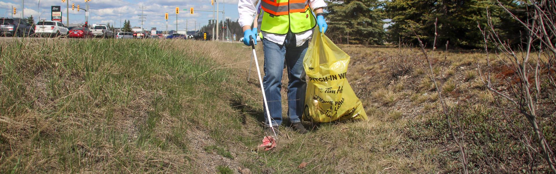 Beside a road, a person is picking up garbage using mechanical grabbing tool.