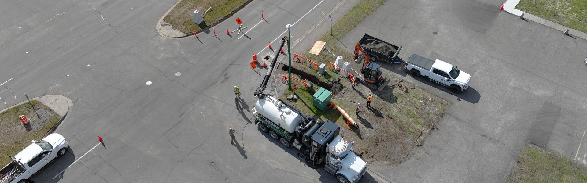 A vac truck and a group of workers installing equipment near a road