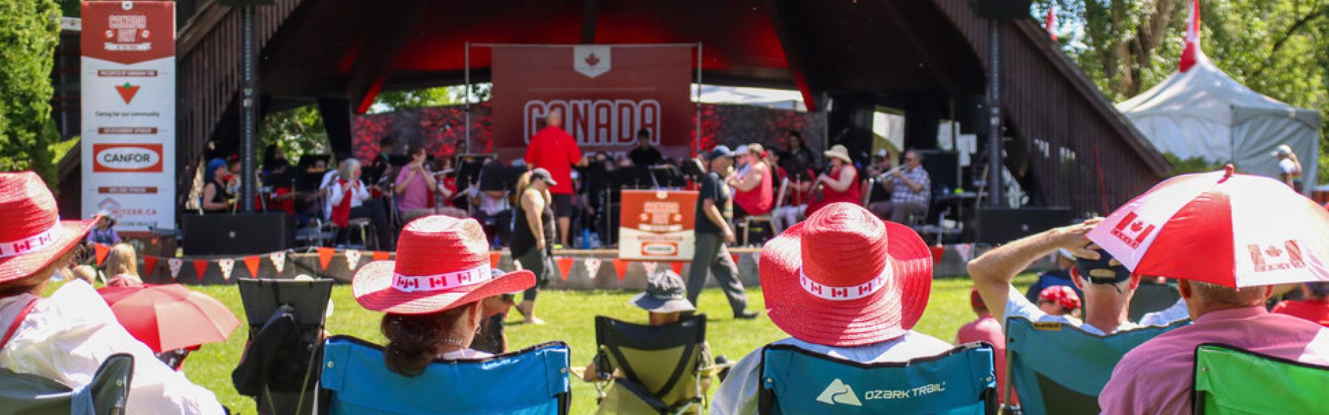 People wearing Canada hats watching entertainment on the stage at Canada Day