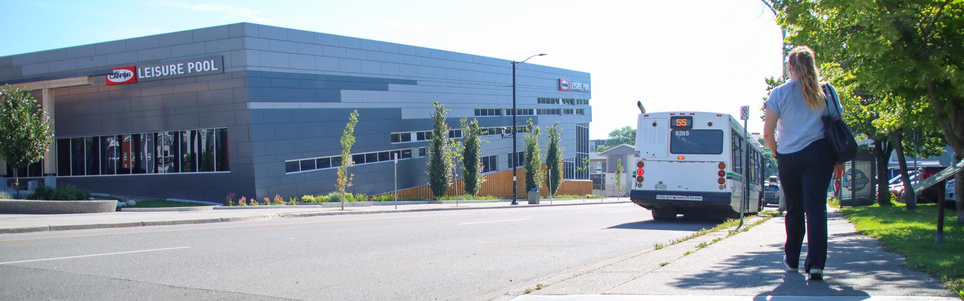 A person is walking down a sidewalk across the street from the Canfor Leisure Pool