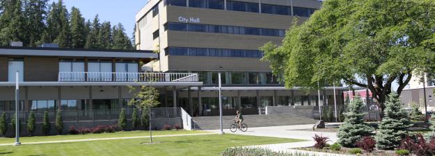 Photo of City Hall with green grass, garden and trees in foreground.