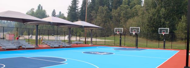 a blue paved basketball court showing some seating on the sidelines