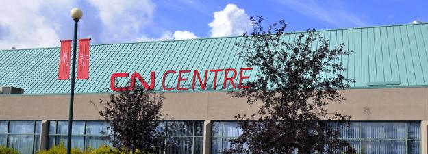 An image of the CN Centre sign next to the box office. A blue sky and clouds are in the background. 