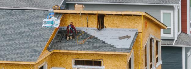 A person working to install a roof onto a new housing development