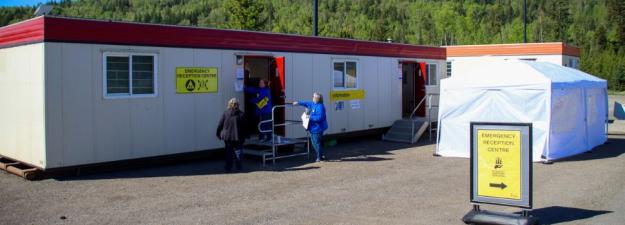 People setting up the emergency reception centre, which includes two trailers and a tent, outside on a sunny day
