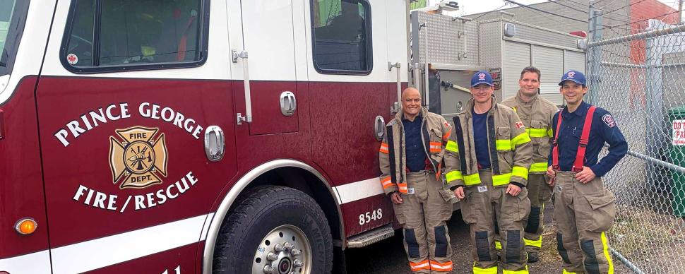 Four firefighters posing alongside a fire truck.