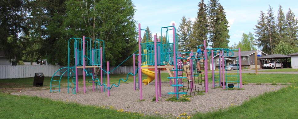 Green and pink playground equipment, with multiple platforms, climbing features, monkey bars, and yellow spiral slide.
