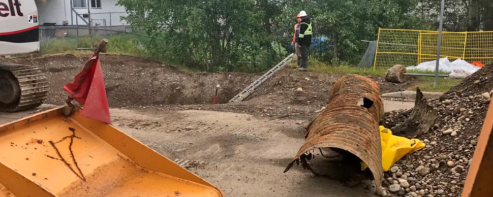 Two workers next to an excavated hole and rusty stormwater culvert.
