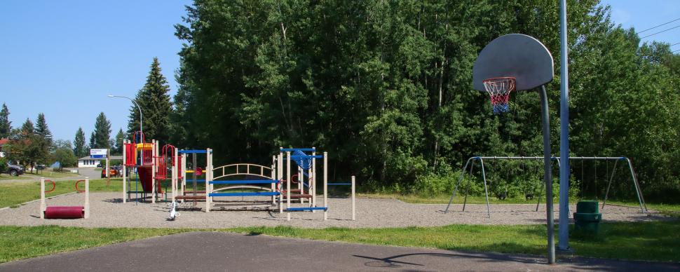 Neighbourhood basketball court with multicoloured playground in background