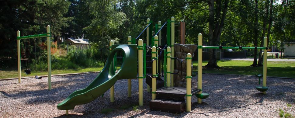 Green and yellow playground equipment surrounded by trees
