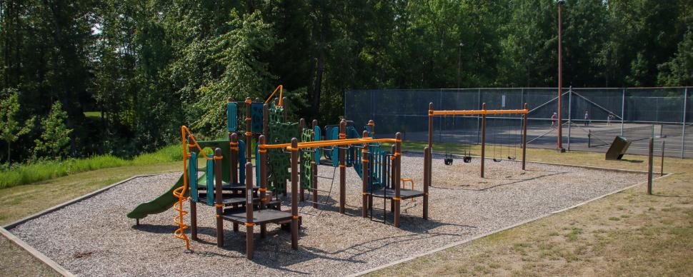 Orange and green playground equipment with tennis courts and trees in the background