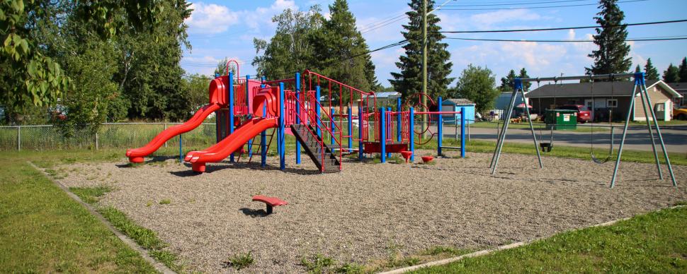 Blue and red playground equipment with swing set surrounded by grass on a sunny day.