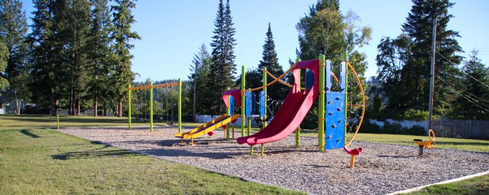 Blue and red playground equipment with swing set surrounded by grass on a sunny day.