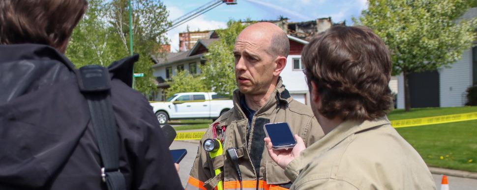 A fire fighter in uniform being interviewed by two reporters