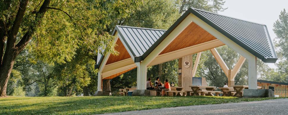 A structure with large angled roof over top of picnic tables