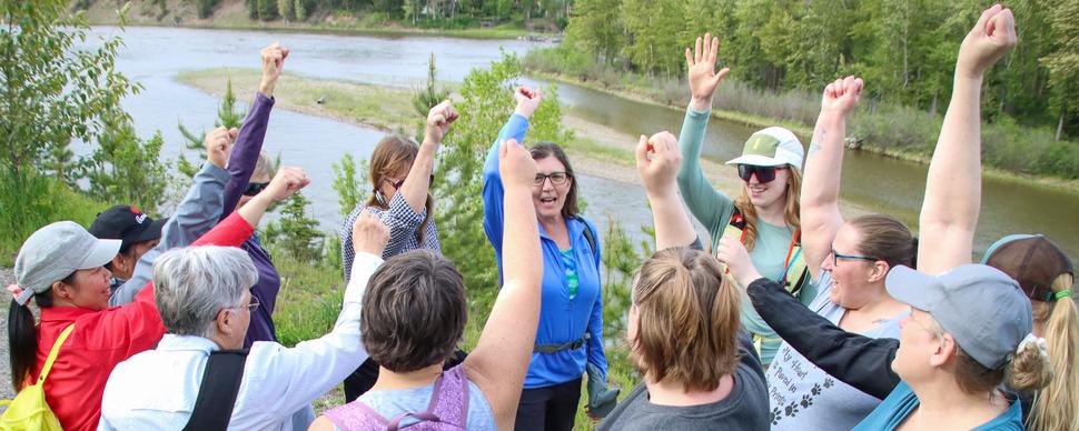A group of women cheering with their arms up next to the Nechako River