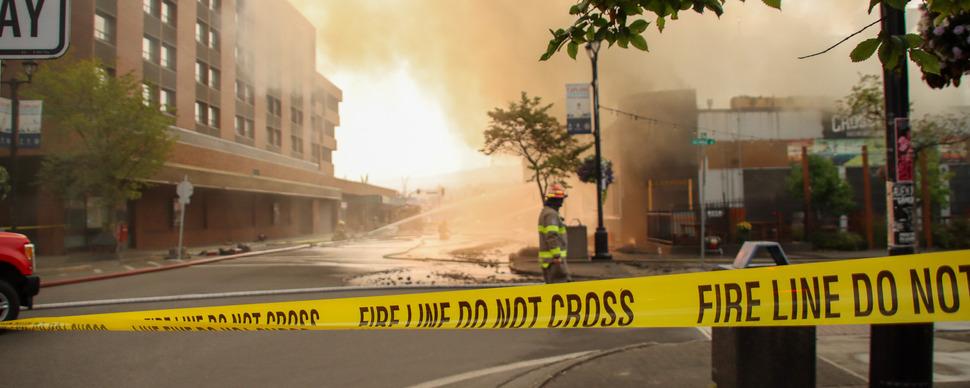 Fire line tape showing smoke and a building being hosed down