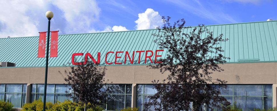 An image of the CN Centre sign next to the box office. A blue sky and clouds are in the background. 