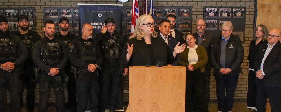 Minister Krieger talking at a podium in front of RCMP members and City Councillors