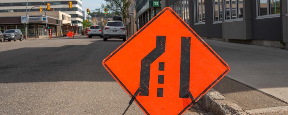 An orange road sign on a downtown road telling drivers to merge into the right lane..
