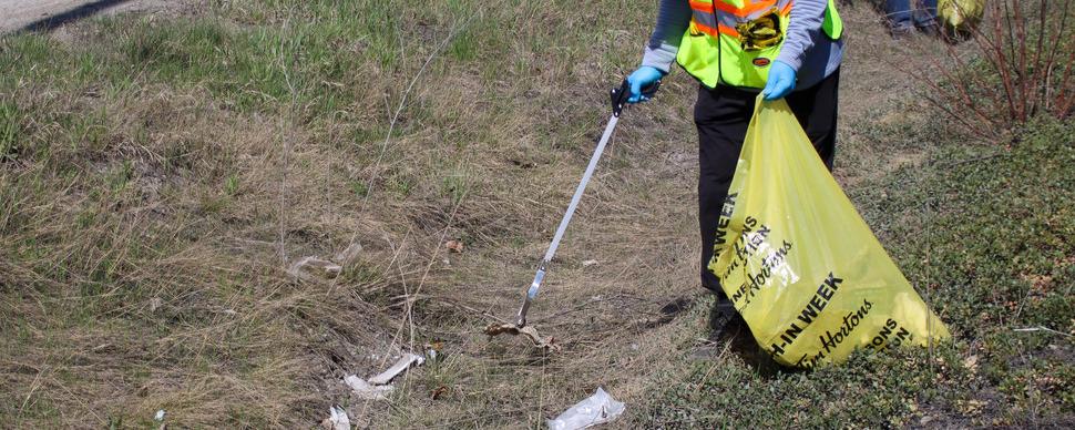A person picking up a piece of garbage with grabbers in one hand and a yellow garbage bag in the other