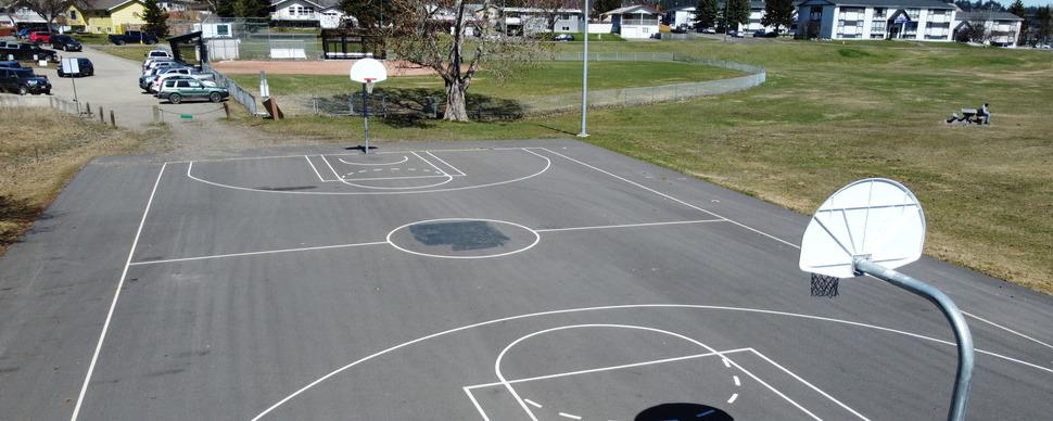 A high angle view of a basketball court with a picnic table. Baseball diamond visible in the distance.