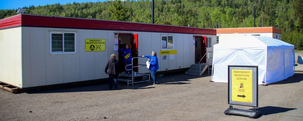 People setting up the emergency reception centre, which includes two trailers and a tent, outside on a sunny day