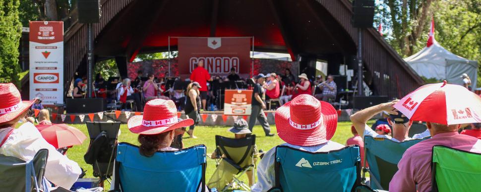 People wearing Canada hats watching entertainment on the stage at Canada Day